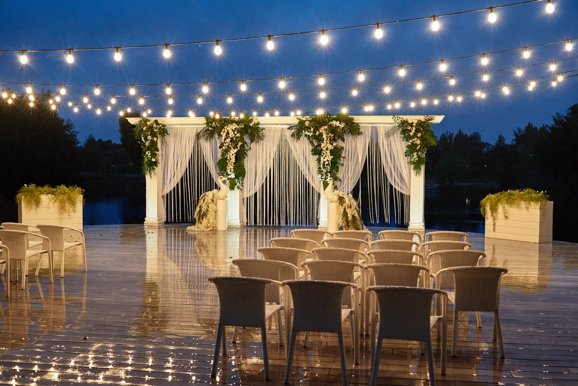 Night wedding ceremony with arch, orchid flowers, chairs and bulb lights in forest outdoors, copy space. Wedding decorations